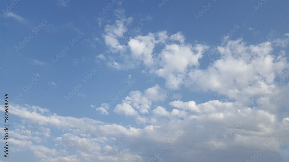 A picturesque natural landscape featuring a vibrant electric blue sky with fluffy white cumulus clouds, stretching towards the horizon over a vast grassland prairie