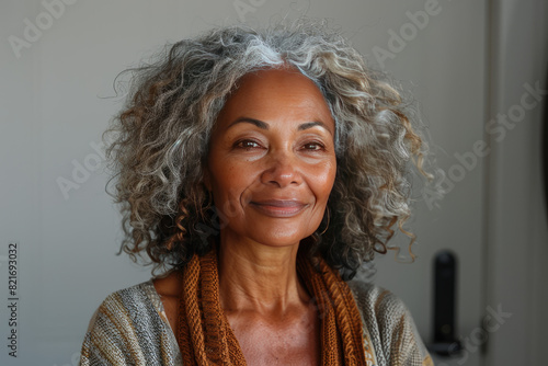 Portrait of a beautiful smiling senior African American woman with curly hair, wearing a casual sweater standing against a grey wall and looking at the camera in a studio. Created with Ai