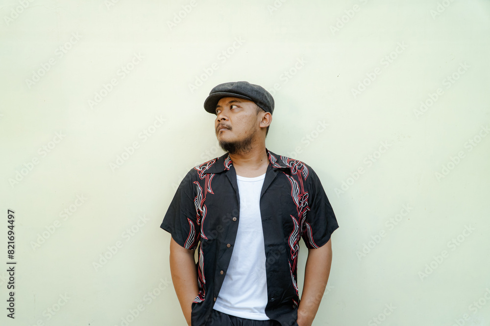 Macho man with beard and mustache looking serious isolated on beige background. Half body portrait of a vintage style Southeast Asian adult man in a patterned shirt, white tank top and newsboy cap Macho man with beard and mustache looking serious isolated on beige background. Half body portrait of a vintage style Southeast Asian adult man in a patterned shirt, white tank top and newsboy cap