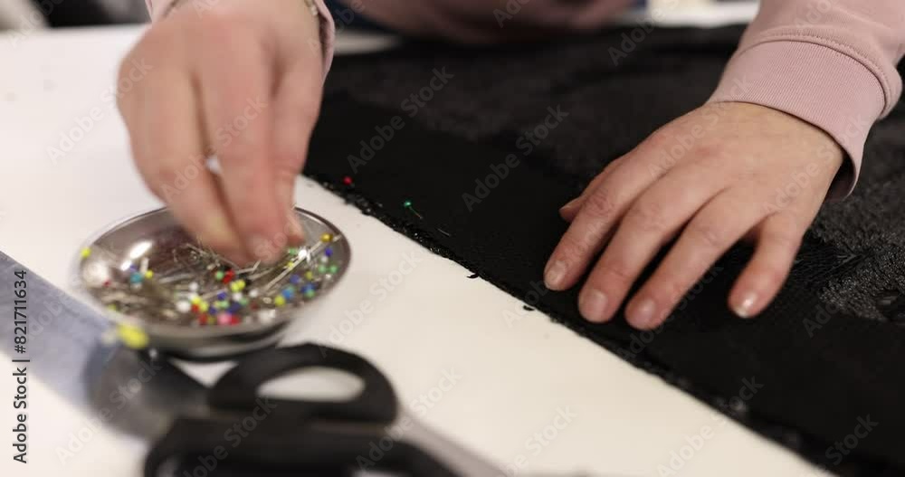 Closeup of seamstress sewing black dress and needle marks into fabric Closeup of seamstress sewing black dress and needle marks into fabric