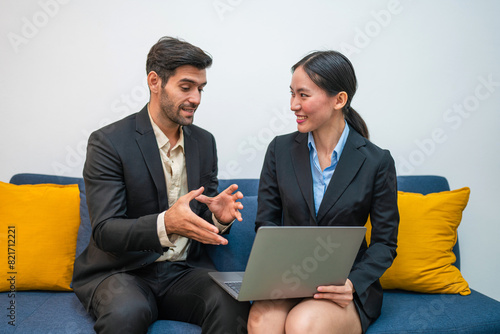 Two happy business woman and man using laptop working on computer at workplace. Cheerful young professional multiethnic colleagues team discussing online digital technology corporate project in office