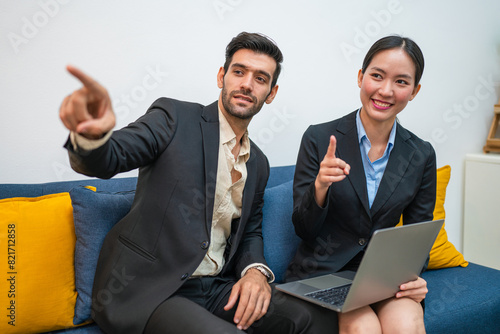 Two happy business woman and man using laptop working on computer at workplace. Cheerful young professional multiethnic colleagues team discussing online digital technology corporate project in office