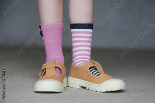 Kid wears different pair of socks. Child foots in mismatched socks standing outdoor.  Down syndrome awareness concept, odd socks day, anti-bullying week. photo