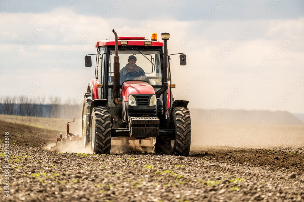 Obraz premium Focused farmer drives a modern tractor to till soil, preparing for sowing season