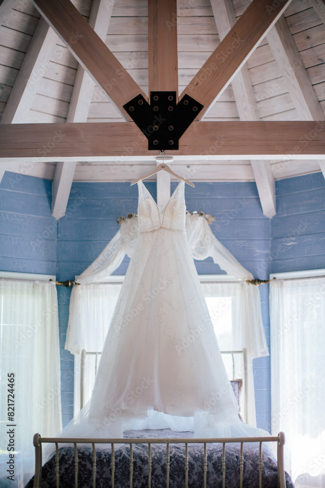 Wedding gown hanging in rustic blue loft with beams Wedding gown hanging in rustic blue loft with beams