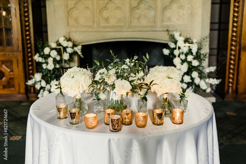 Table with white roses and gold votive candles in front of a fireplace