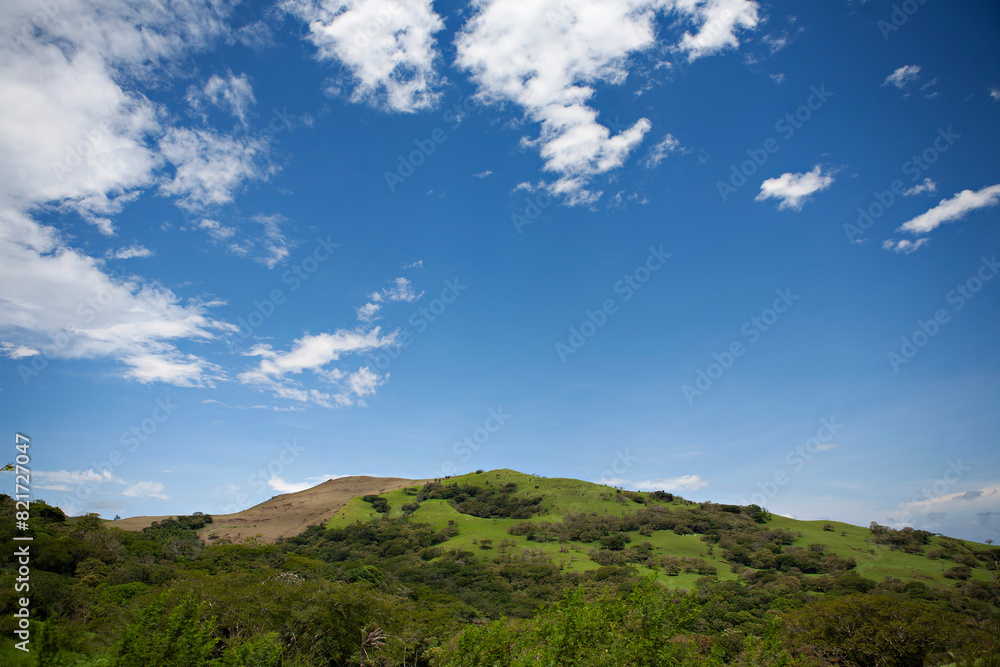 Lush green hills under a blue sky with clouds in Costa Rica.
