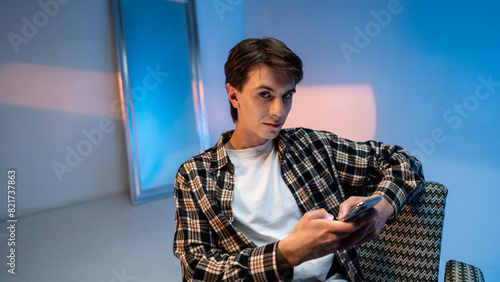 Handsome trendy young model sitting in a armchair and browsing on her mobile phone at the studio