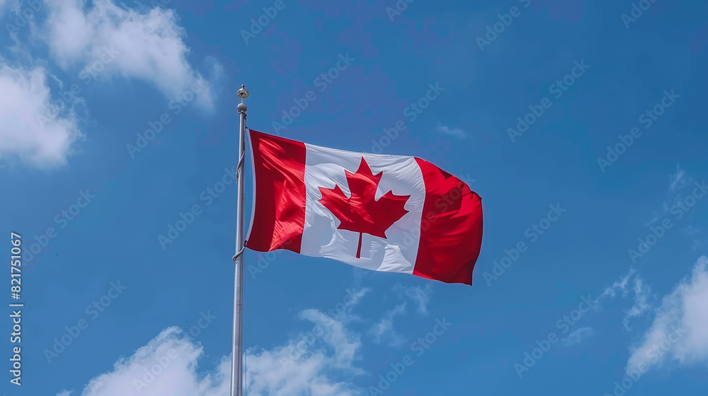 The Canadian flag on a flagpole flutters in the wind against a blue sky The Canadian flag on a flagpole flutters in the wind against a blue sky