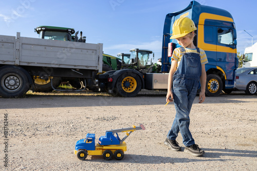 7-year-old boy plays with a toy car, and behind him are large cabins of commercial vehicles. interesting childhood of a child, games in the profession. The boy's interest in machines and their work.