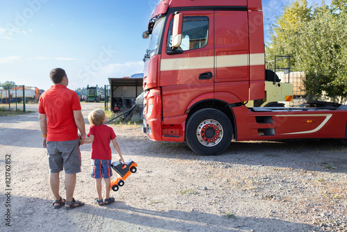 boy and a man standing with their backs against the backdrop of the cab of a tractor-trailer examine the cars with interest. Spend the day with your son. The boy's interest in machines and their work