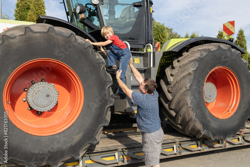 boy climbs onto a huge tractor wheel, his dad helps him. Spend the day with your son. Interest in machines and their operation. interesting childhood. Contrast sizes