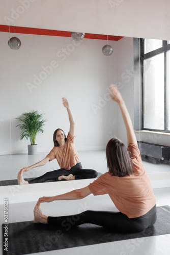 woman in front of mirror does stretching, practices yoga and meditation in gym. Taking care of physical and mental health. European person at sports training session