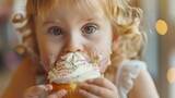 Sweet tooth Child Bites into Muffin with Sugary Frosting. Adorable Little Girl Eats Creamy Cupcake with Frosting and Sprinkled Confetti. Shot with Warm Light Filter.