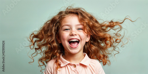Cute young child Little girl smiles. Emotion and child development. Little girl smiles while red hair. A young girl with curly hair is smiling and laughing while wearing a shirt.