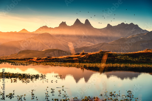 Sunrise shines over Lac Guichard with bird flying on Arves massif and lake reflection at Aiguilles d'Arves, French Alps, Savoie, France photo