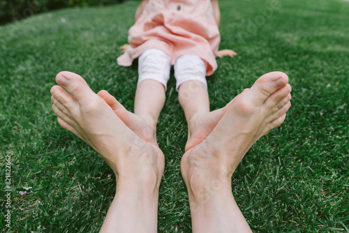 Mother joining feet with daughter sitting on grass at park photo