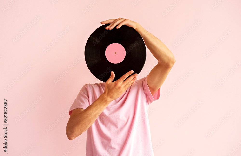 © dvulikaia - Portrait of man in pink shirt holding vinyl record near his face on pink background.