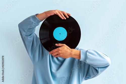 Man in  blue sweatshirt covers his face with vinyl record on blue background