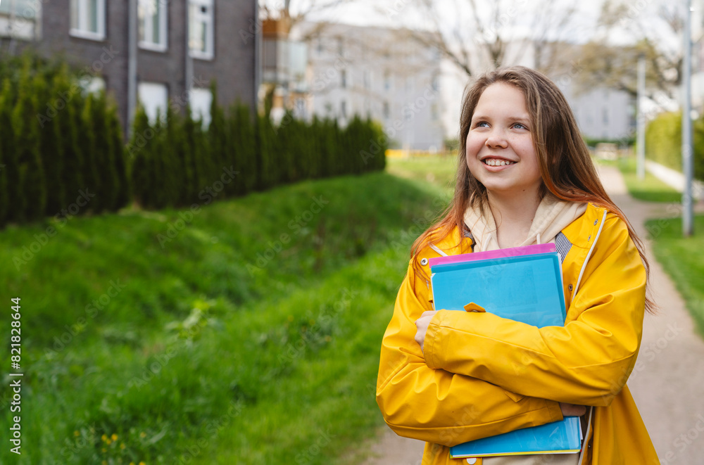 Smiling girl holding folders and standing on footpath Smiling girl holding folders and standing on footpath