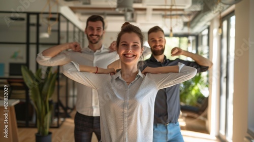 Team of three corporate business people doing sports exercises at the office. Smiling young woman and two men standing at the office stretching their shoulders.