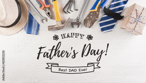 Happy Father's Day decoration with beautiful tie with mustache, hand tools, glasses, gift box and hat on white wooden background.