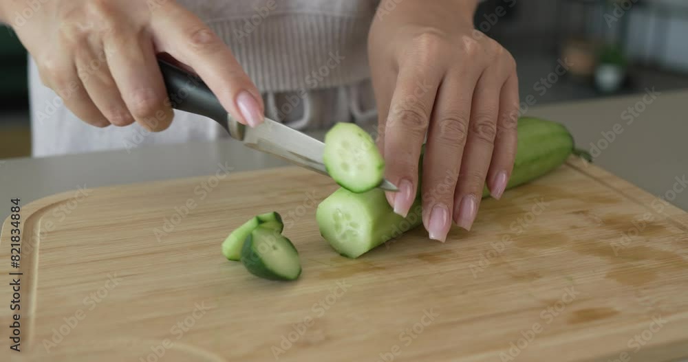 An unknown adult caucasian woman stand and cut cucumber at home An unknown adult caucasian woman stand and cut cucumber at home