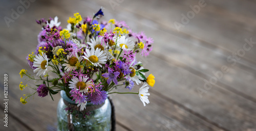 Wildflowers in a glass vase on rustic wooden table in summer - garden feeling, summertime concept