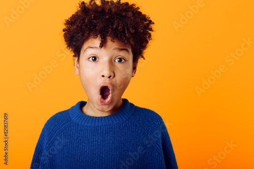 Young african american boy wearing bright colors expresses astonishment with wideopen mouth against a vivid orange backdrop photo
