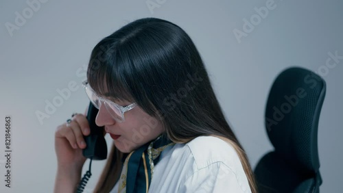 Beautiful young woman with long dark hair wearing glasses talking on the phone with a client and hanging up in slow motion. Woman working hard in office. photo