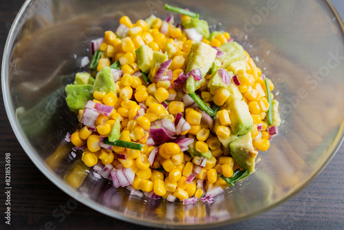  vibrant colors of a summer salad featuring corn, red onion, and avocado, drizzled with lime dressing, presented in a glass bowl in this closeup