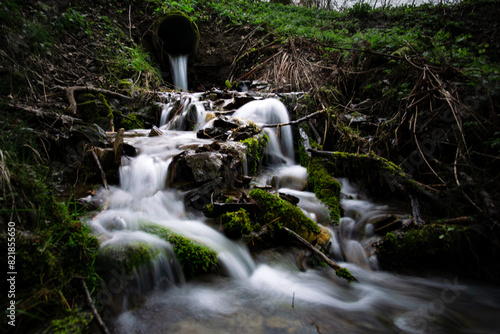 In the woods, a pipe releases water forming a beautiful waterfall