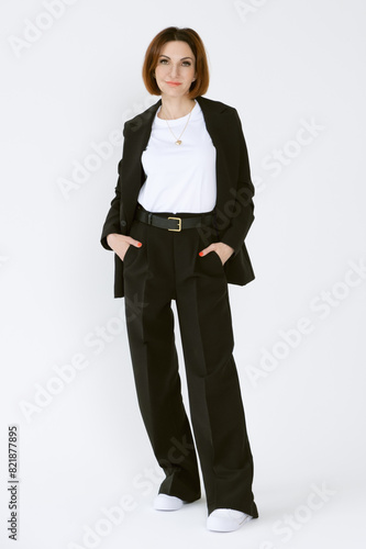 Portrait of a confident business woman in a black pantsuit and a white blouse on a white background. Full-length portrait of a middle-aged woman in black trousers