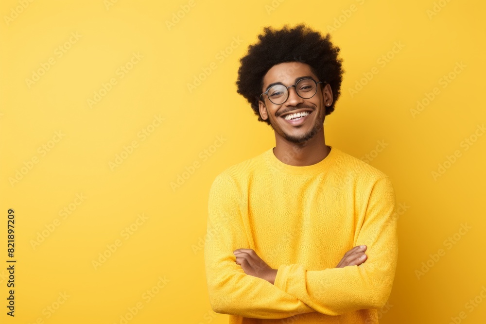 Obraz premium Portrait of a joyful afro-american man in his 20s with arms crossed while standing against pastel yellow background