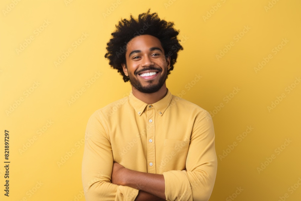 Portrait of a joyful afro-american man in his 20s with arms crossed in front of pastel yellow background Portrait of a joyful afro-american man in his 20s with arms crossed in front of pastel yellow background