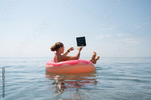 Woman laptop sea. Freelancer woman in sunglases floating on an inflatable big pink donut with a laptop in the sea. People summer vacation rest lifestyle concept photo
