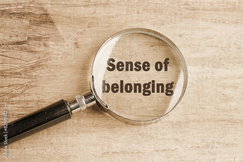 Business, sense of belonging concept. Text Sense of belonging visible through a magnifying glass on an old faded background © Ihar