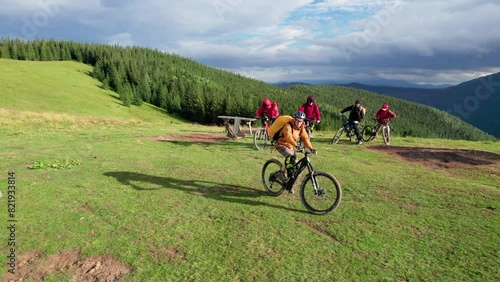 Group of cyclists men riding electric bikes outdoors. Aerial view of male tourists biking on grassy trail in the mountains at summer. Concept of sport, active leisure and nature.