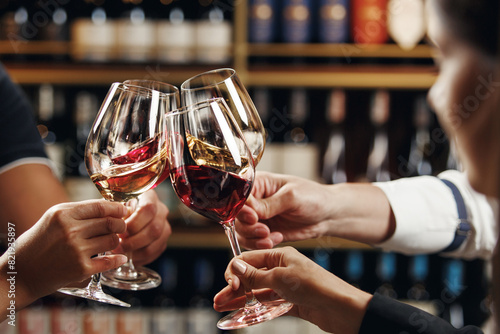 Big company people clinking glasses with red, rose and white wine on blurred cellar background. Men and women cheers with alcohol drink, closeup