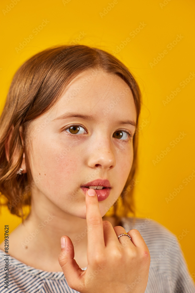 A teenage schoolgirl with a contemplative look touches her lips against a vibrant yellow backdrop. A teenage schoolgirl with a contemplative look touches her lips against a vibrant yellow backdrop.