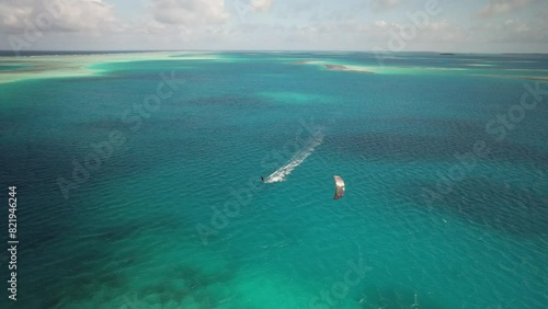 A kite surfer on vivid blue waters with a boat nearby, sunny day, aerial view