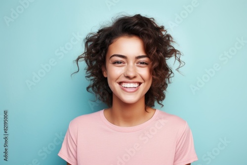 Portrait of a grinning woman in her 20s smiling at the camera in front of solid pastel color wall