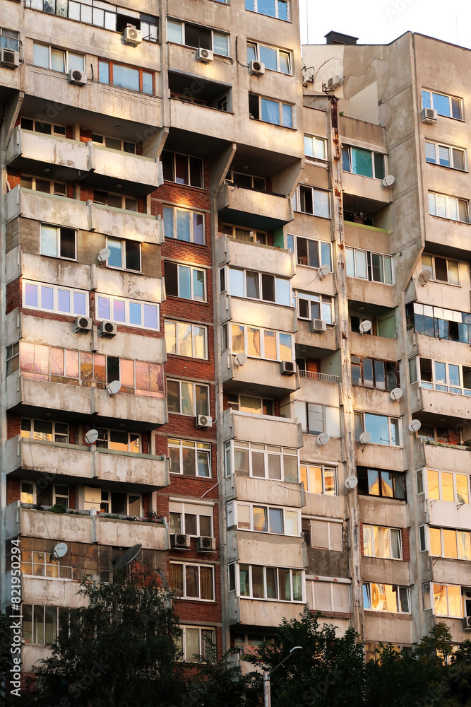 Obraz premium The sunset reflecting in orange, yellow, pink in the many windows of a concrete, socialist, brutalist panel, multi-story, high-rise, apartment block, building, Sofia, Bulgaria