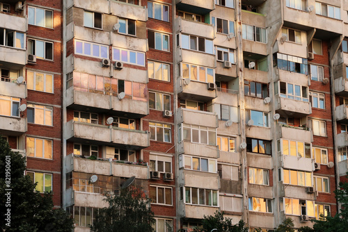 The sunset reflecting in the many windows of a concrete, socialist, brutalist panel, multi-story, high-rise, apartment block, building, orange, yellow, pink reflection, Sofia, Bulgaria