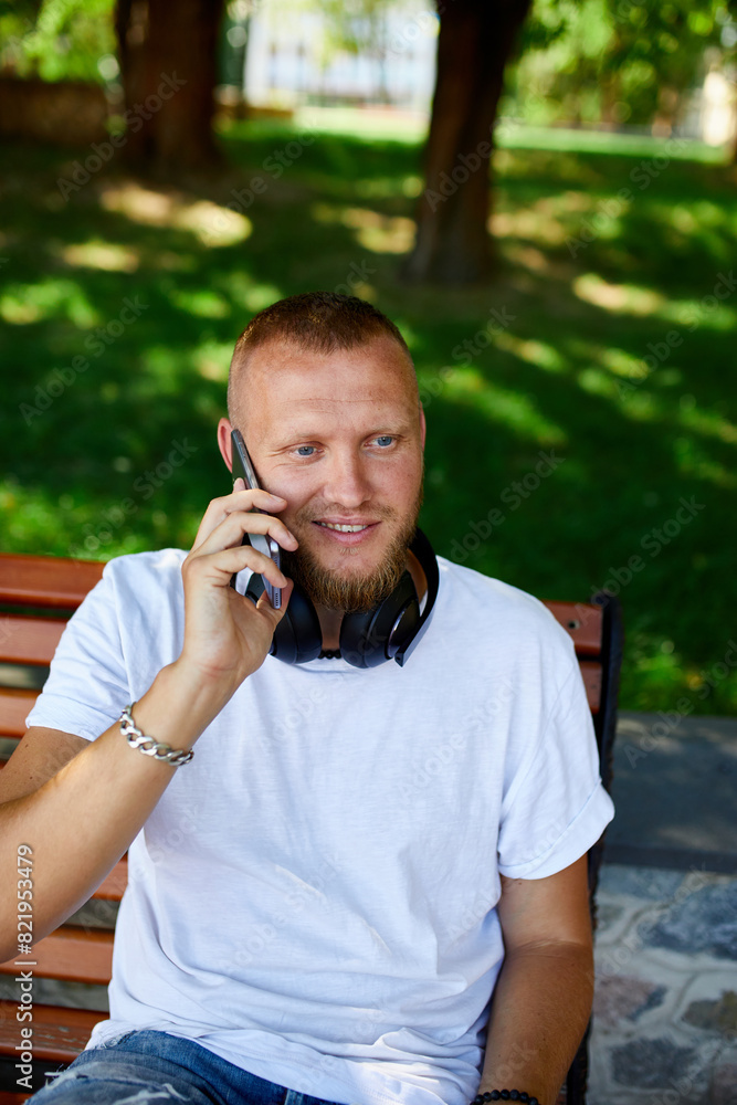 Smiling Man With Headphones Talking on Phone in Sunny Park Smiling Man With Headphones Talking on Phone in Sunny Park
