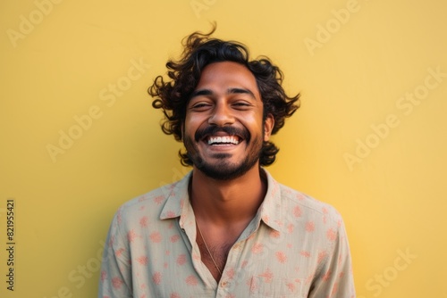 Portrait of a joyful indian man in his 20s smiling at the camera while standing against solid pastel color wall
