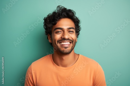 Portrait of a smiling indian man in his 20s smiling at the camera on solid pastel color wall © Markus Schröder