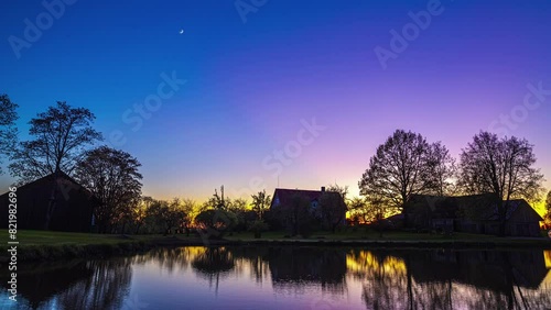 Day to night timelapse with sunset and moonset above cottage near pond photo