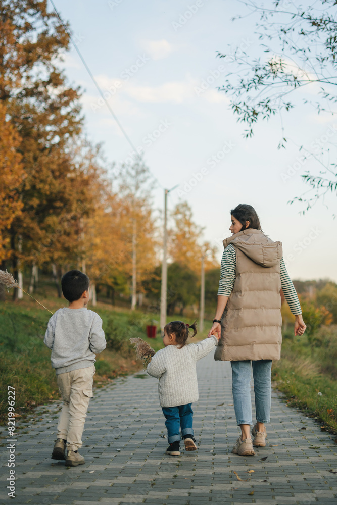 Back view of a woman walking down the path with her two kids. Daughter holding onto his mother's hand tightly, feeling safe in her embrace. Back view of a woman walking down the path with her two kids. Daughter holding onto his mother's hand tightly, feeling safe in her embrace.
