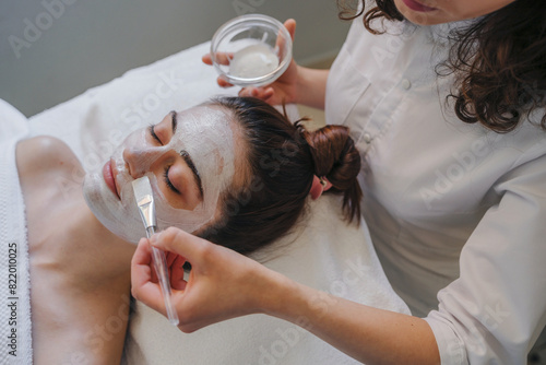 Spa therapy for young woman receiving facial mask at beauty salon - indoors. Dermatologist make beauty procedures for woman patient in aesthetic medical clinic